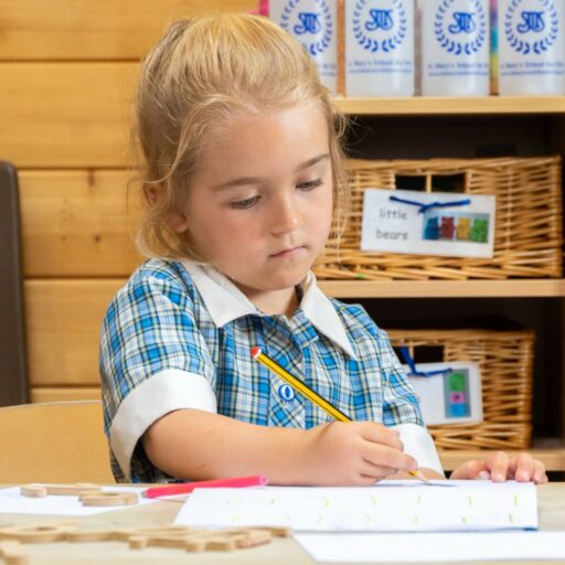 Kindergarten pupil sitting at a desk in a classroom practicing her letter formation in a preschool setting at St Mary's