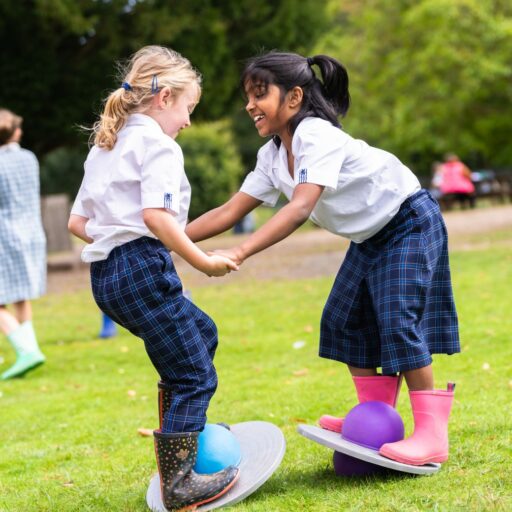 Two girls laughing while playing in an outsite area with wobble boards and strengthening their gross motor skills at St Mary's school