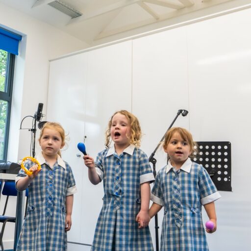 Three girls singing and playing instruments at a preschool music lesson at st mary's Kindergarten in Colchester, essex