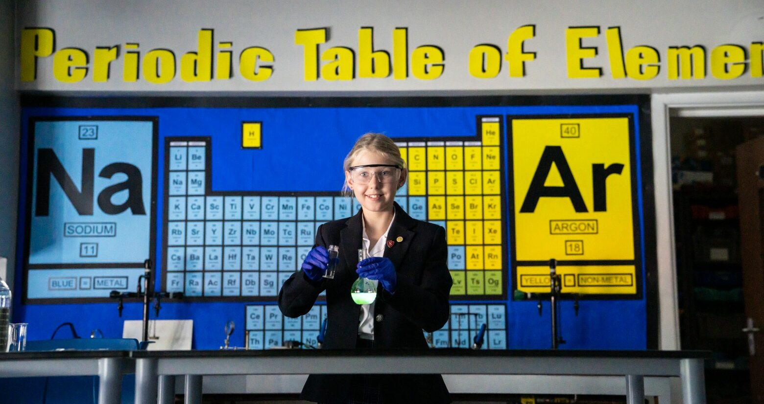 Senior school pupil in a science lab at St Mary's school conducting an experiment while standing in front of of a periodic table