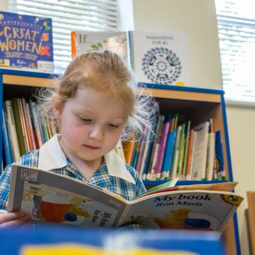Preschool girl reading a book in the library at the Lower school at St Mary's Colchester