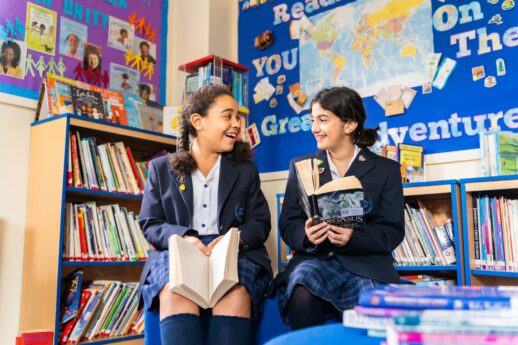 Two St Mary's Lower School pupils sitting in a Library holding books and laughing